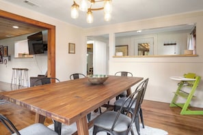 A dining area with a wooden table, chairs, a bowl, and a green high chair. - 11th Street River House | Walk to Town | On River (Bandera)