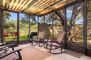 Un patio cubierto con vistas a un jardín trasero, con mecedoras y una parrilla.