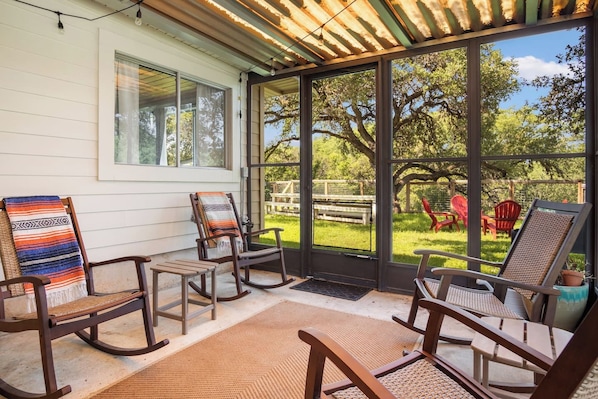 A covered porch with rocking chairs and a view of a backyard.