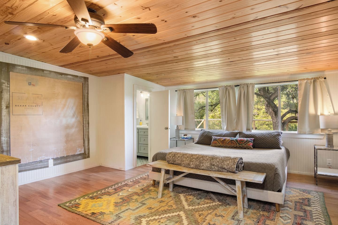A bedroom with a wooden ceiling, a bed with a headboard, a window with curtains, and a nightstand.