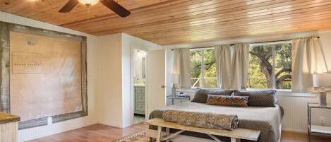 A bedroom with a wooden ceiling, a bed with a headboard, a window with curtains, and a nightstand.