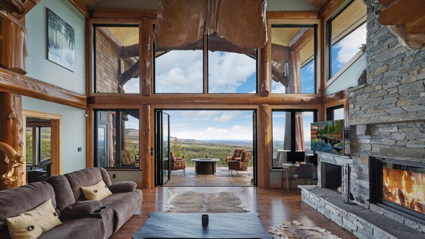 A spacious living room with a stone fireplace, large windows, and a view of the landscape.