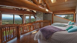 A bedroom with a large bed, wooden beams, stone wall, and a view of the forest.