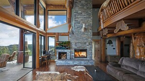 A spacious living area with a stone fireplace, wooden furniture, and a large window overlooking a scenic landscape.