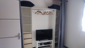 A bedroom with a wardrobe, a bed, and a television on a stand.