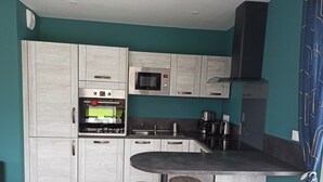 A modern kitchen with light wood cabinets, a built-in microwave, a coffee maker, and a bar area with stools.