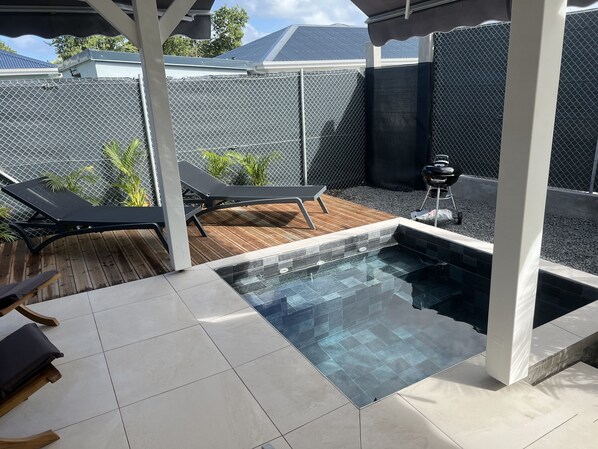 Un jardin avec une piscine, des chaises longues et un barbecue.