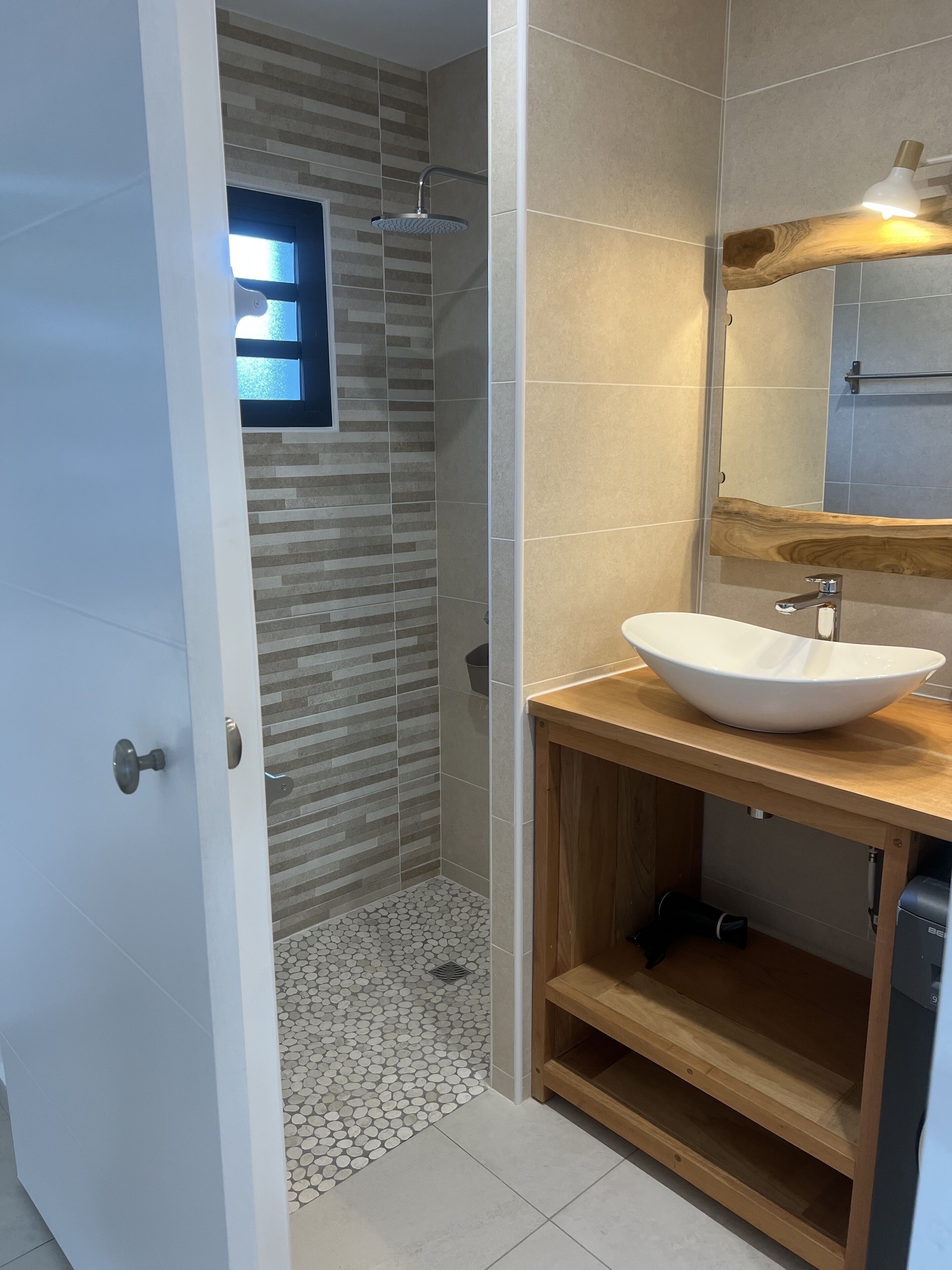 Une salle de bain moderne avec une douche, un lavabo blanc et un meuble-lavabo en bois.