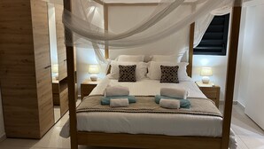 Un lit à baldaquin avec des rideaux, une literie blanche et de nombreux oreillers. Il y a des tables de chevet avec des lampes et une armoire en bois.