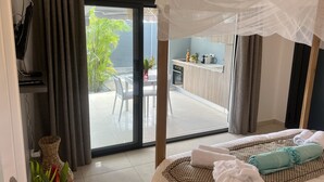 Une chambre d’hôtel avec un lit, une petite kitchenette, un balcon agrémenté de plantes et une vue sur l’extérieur.