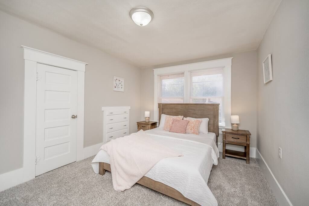 Une chambre à coucher comprenant un lit, une table de chevet, une commode, une fenêtre et une porte.