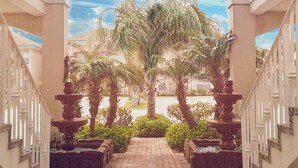 A covered walkway with a brick floor, flanked by white railings and palm trees.