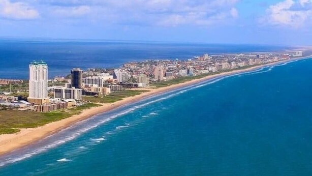 A coastal cityscape with a prominent high-rise hotel and a beach.