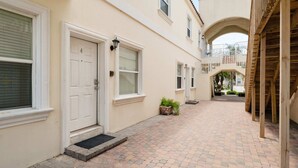 A narrow, paved courtyard with a white door and windows, leading to a wooden staircase.