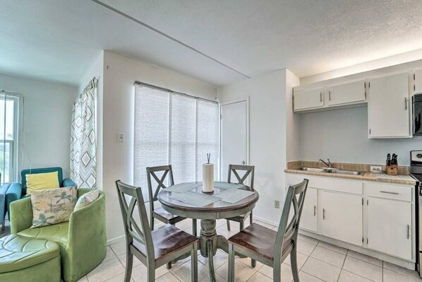A modern kitchen with white cabinets, a dining table with chairs, and a small seating area with a green sofa.