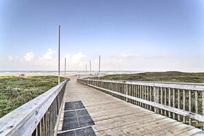 A wooden boardwalk leading to a beach with a grassy area on one side and a wooden fence on the other.
