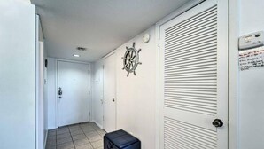 A hallway with a closed door, a wall-mounted ship's wheel, and a suitcase on the floor.