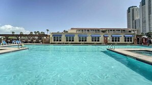 A swimming pool with lounge chairs and a building with blue awnings in the background.