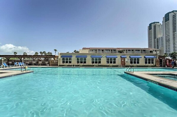 Una piscina con sillas de descanso y un edificio con toldos azules al fondo.