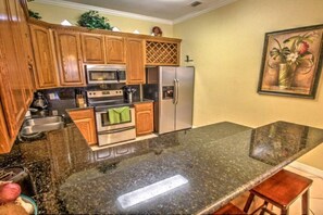 A kitchen with wooden cabinets, stainless steel appliances, a granite countertop, and a painting on the wall.