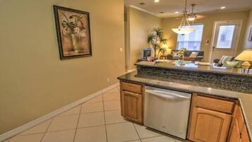 A kitchen with a granite countertop, wooden cabinets, and a dishwasher. There is a painting on the wall and a window with blinds.