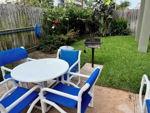 Un patio con una mesa redonda blanca y sillas azules, una parrilla y una valla de madera.