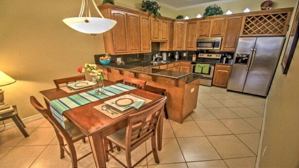 A kitchen with wooden cabinets, a stainless steel refrigerator, and a dining area with a table set for two.