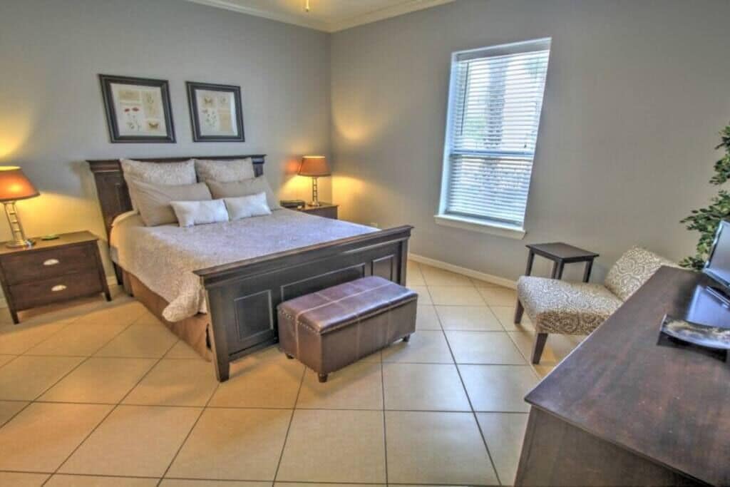 A bedroom with a large bed, bedside tables, a bench, a chair, and a window.