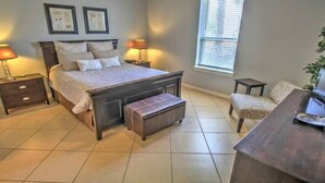 A bedroom with a large bed, bedside tables, a bench, a chair, and a window.