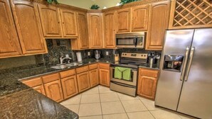 A kitchen with wooden cabinets, granite countertops, stainless steel appliances, and a tiled floor.