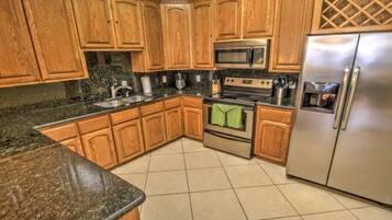 A kitchen with wooden cabinets, granite countertops, stainless steel appliances, and a tiled floor.