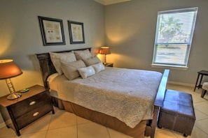 A bedroom with a bed, nightstands, a lamp, a window with blinds, and a small bench.