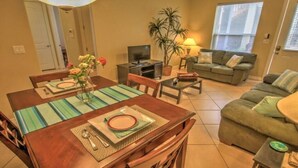 A living room with a sofa, a TV, a dining table with chairs, and a plant.