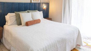 Una cama bien hecha con edredón blanco, varios almohadones y cabecera azul.