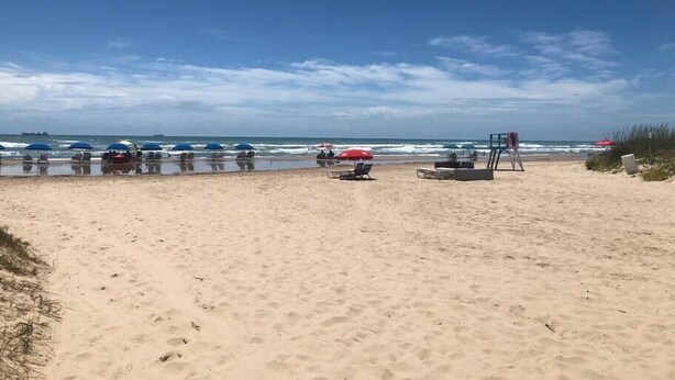 Una playa con sombrillas y sillas de descanso, una torre de salvavidas y el océano al fondo.