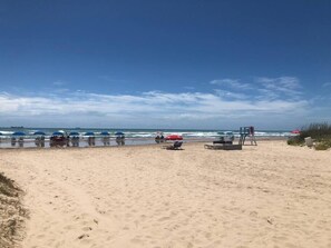 A beach with umbrellas and lounge chairs, a lifeguard tower, and the ocean in the background.