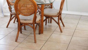 Un comedor con una mesa de vidrio rodeada de sillas de mimbre, una lámpara colgante y una planta grande de hojas anchas.