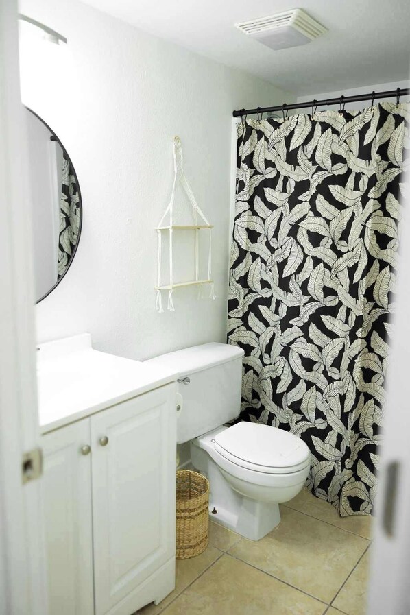 A bathroom with a toilet, a white sink, a mirror, and a shower curtain with a leaf pattern.