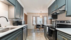 Een moderne keuken met donkere kastjes, een centraal eiland en een eetgedeelte met een kroonluchter.