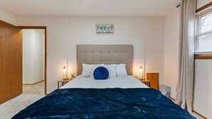 Een slaapkamer met een groot bed, twee nachtkastjes, een hoofdbord en een raam met gordijnen.