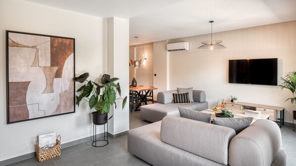 Una sala de estar moderna con un sofá gris, una zona de comedor con mesa de madera y un cuadro abstracto grande en la pared.