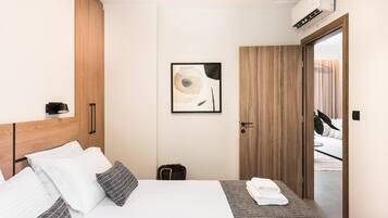 A modern hotel room with a wooden headboard, a bed with white and patterned bedding, a small bedside table with a lamp, and a framed abstract artwork on the wall.