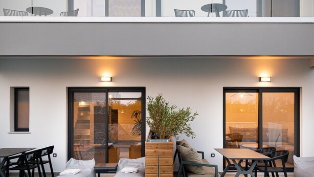 Un bâtiment moderne à deux étages doté d’une piscine, d’un espace extérieur aménagé et de plantes en pot.