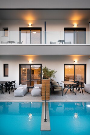 Un moderno edificio de dos plantas con piscina, mobiliario exterior y una planta en maceta.