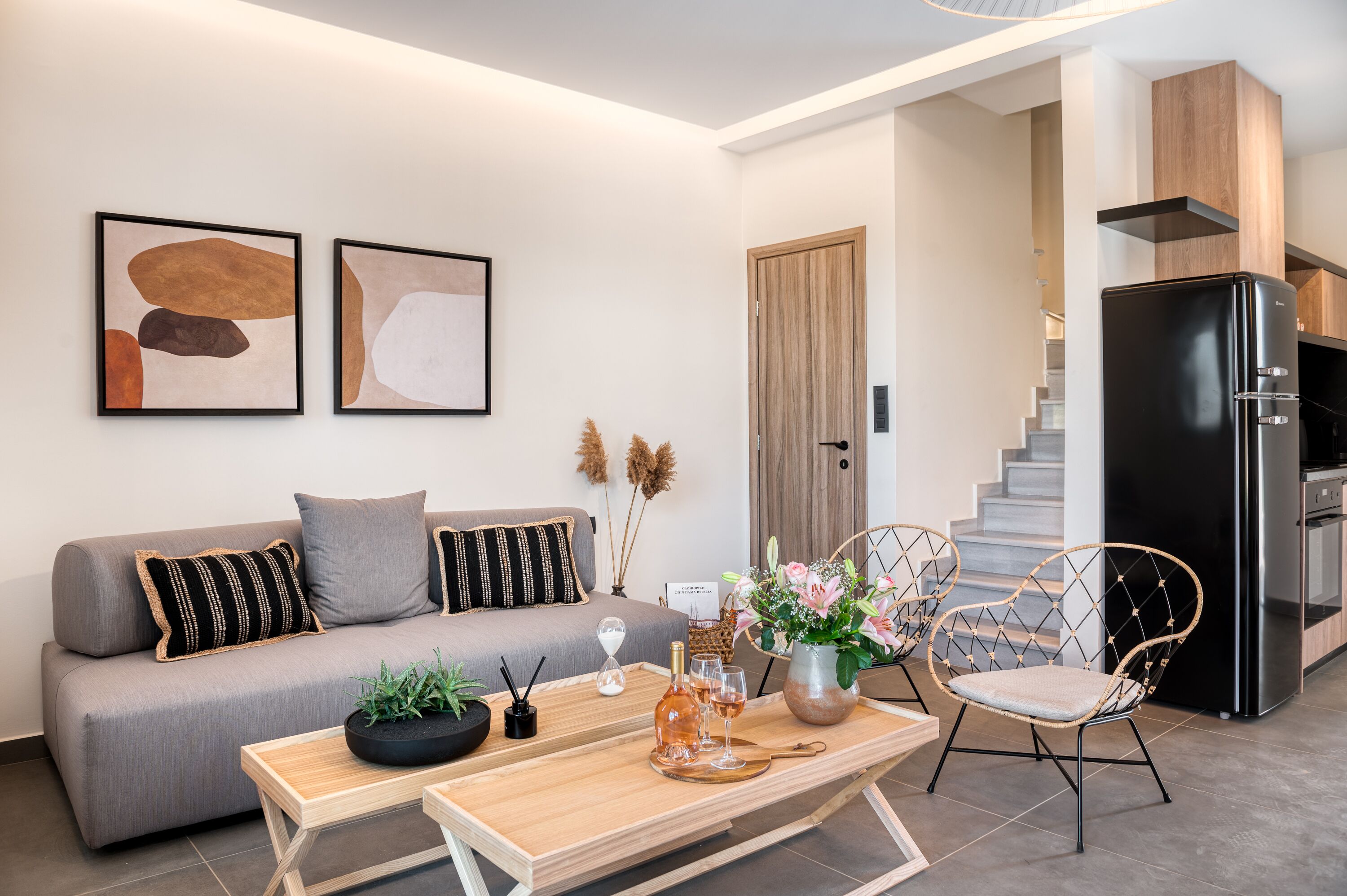 Una sala de estar moderna con sofá, una mesa de centro y objetos decorativos. Una escalera conduce a una zona de cocina con un refrigerador.