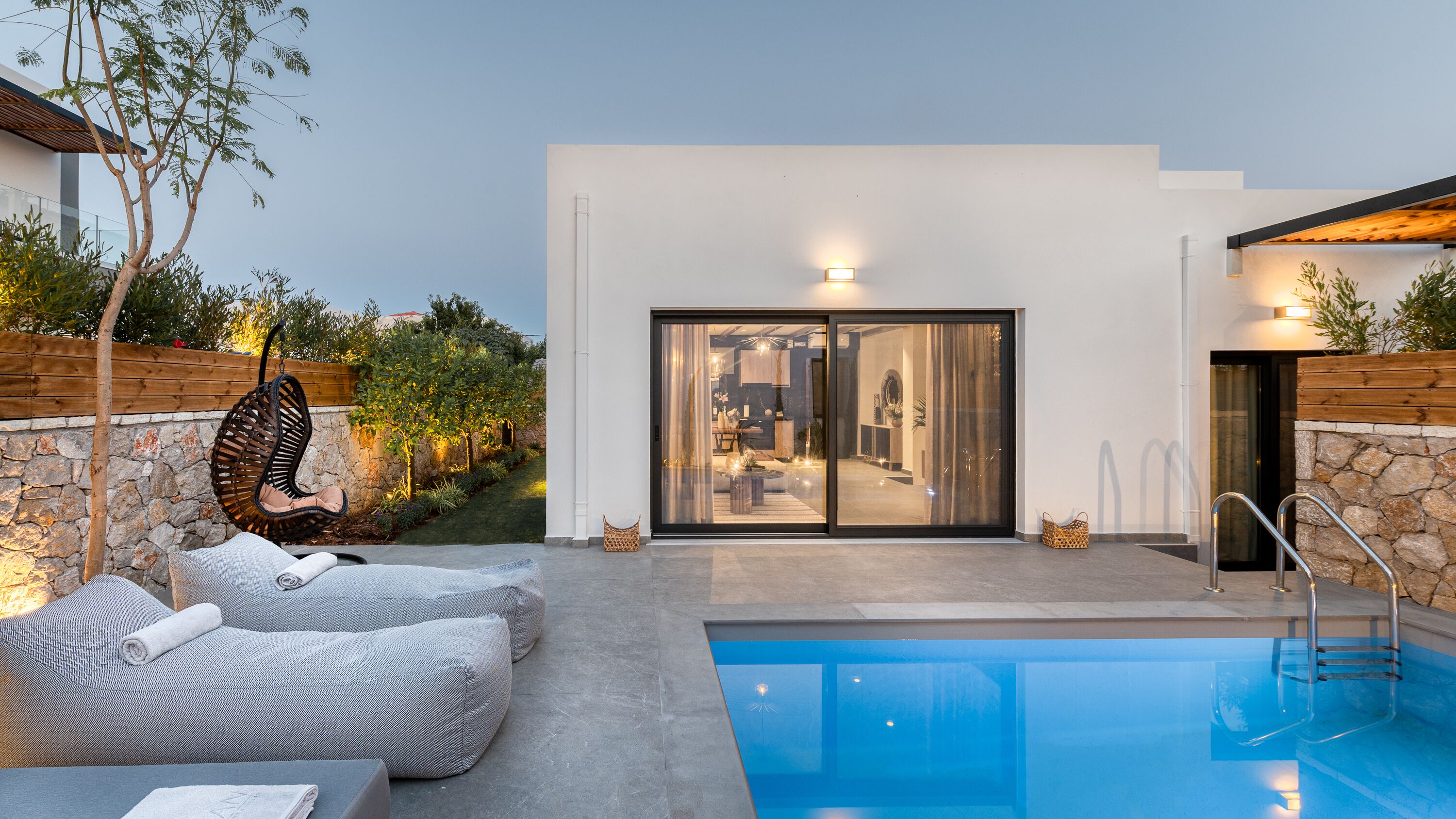 A modern outdoor pool area with a glass door entrance, stone walls, and a seating area with cushions.