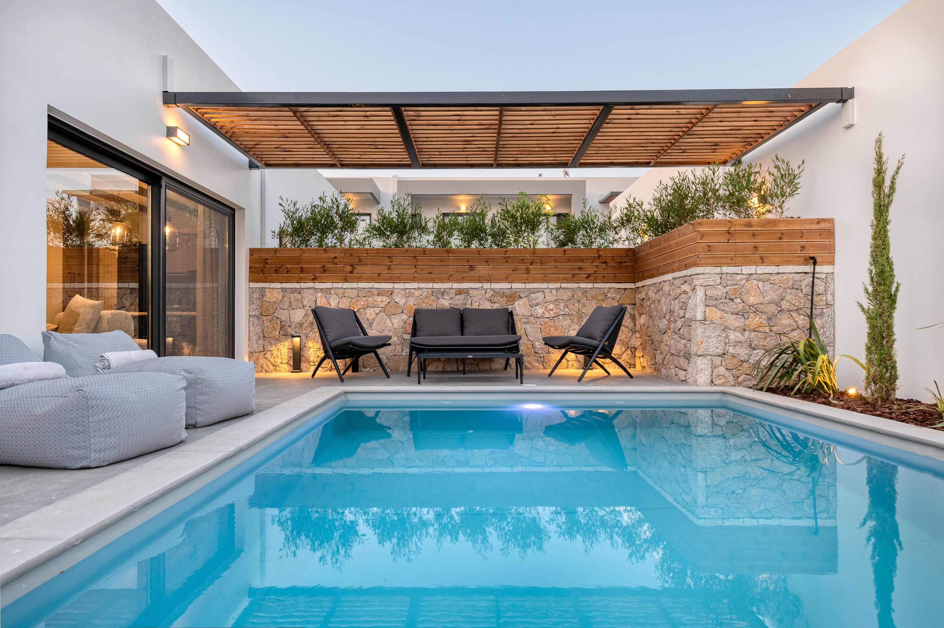 A modern outdoor pool area with a stone wall, wooden deck, and two lounge chairs.