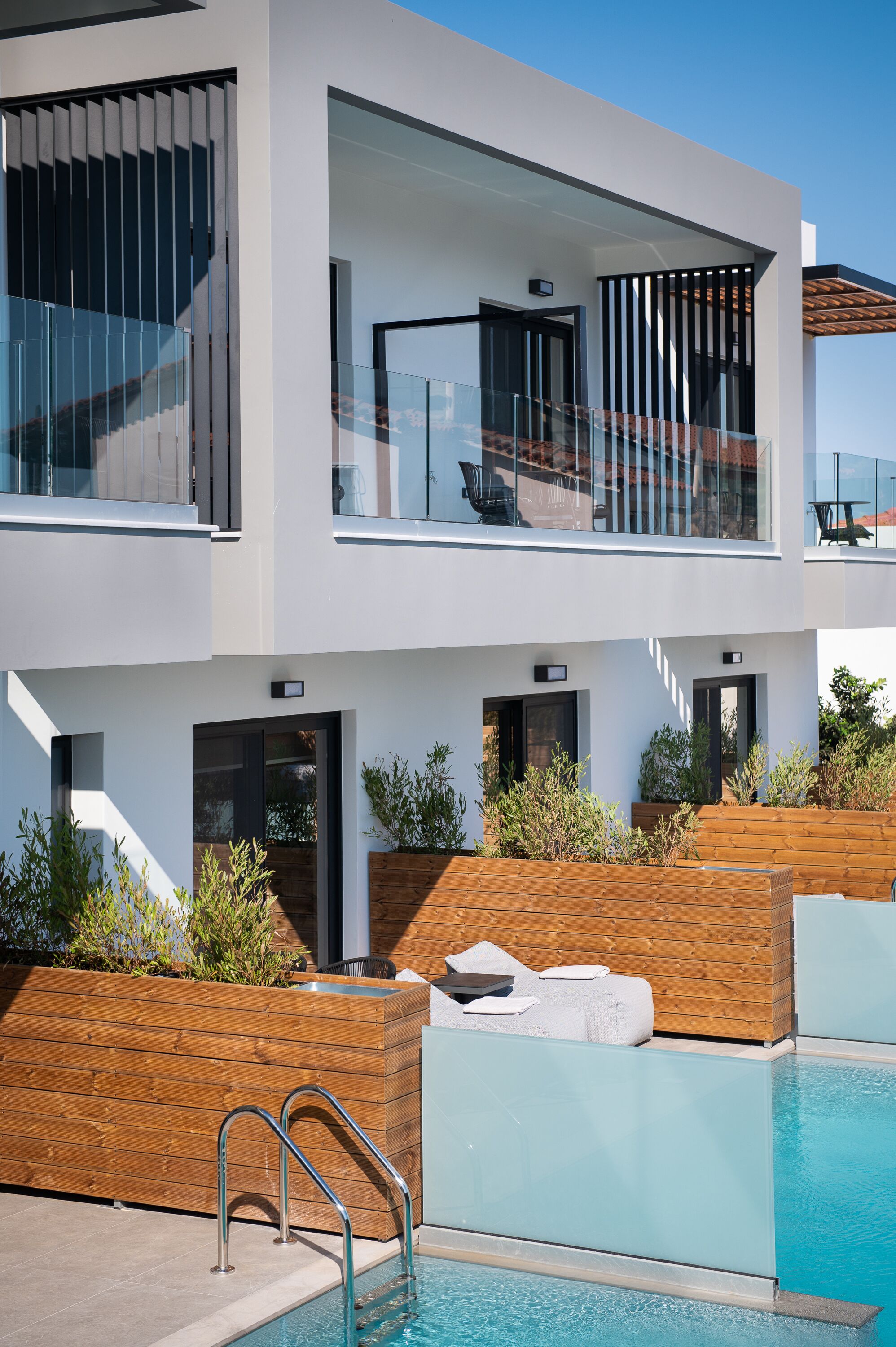 Een modern huis met twee verdiepingen, een zwembad, een houten terras en een zitgedeelte buiten.