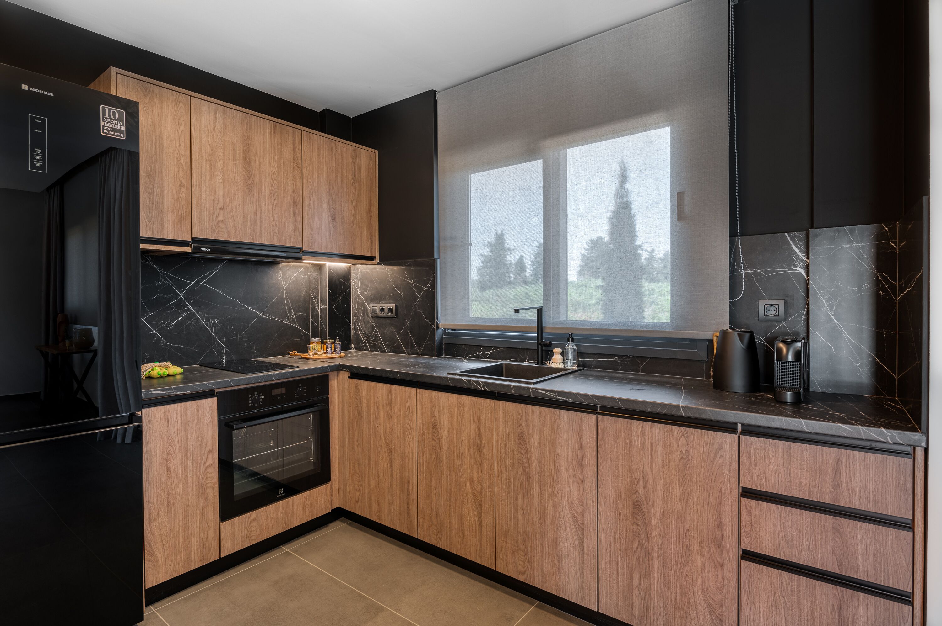 A modern kitchen with wooden cabinets, a black countertop, and a window with a view of trees.