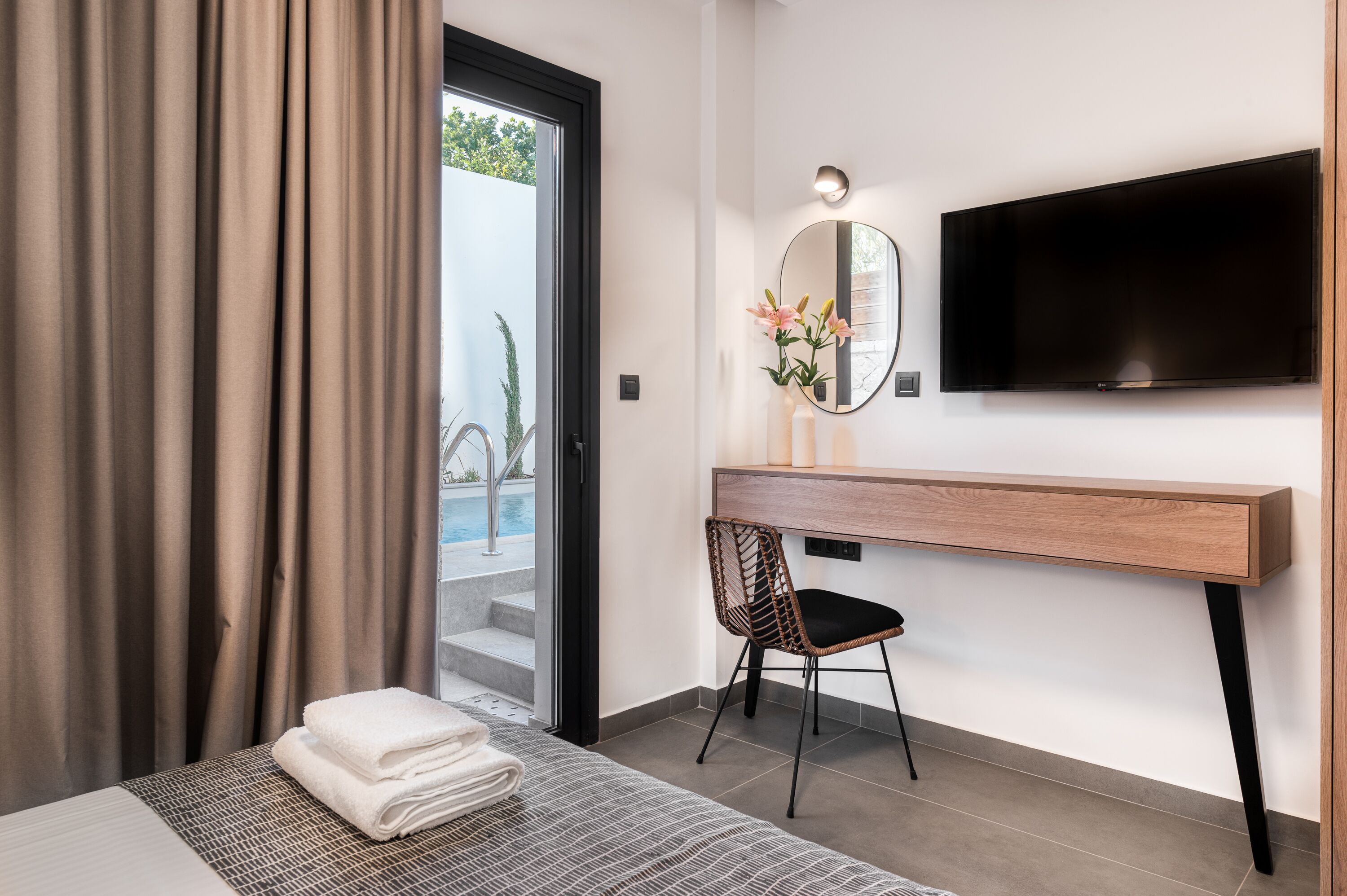 Ein modernes Hotelzimmer mit Bett, Schreibtisch mit Stuhl, Fernseher und Blick ins Freie.